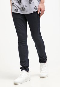 Dark denim skinny jeans with a smooth texture, paired with white sneakers featuring a textured design and round toe.