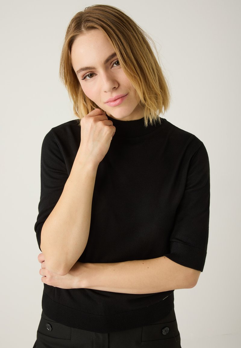 Schwarzes Strickoberteil mit hohem Kragen und kurzen Ärmeln. Das Material scheint weich zu sein und hat ein figurbetontes Design mit gerippten Akzenten an den Bündchen und am Saum.