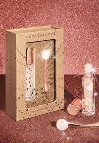 Un set di occhi 3D in quarzo chiaro racchiuso in una scatola dorata comprende una bottiglia di siero in vetro, un applicatore in rosa oro con una pietra bianca e decorazioni di glitter.
