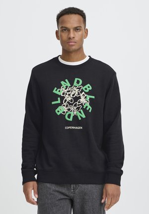 Hombre que lleva una sudadera negra con texto verde y diseño floral que dice "BLEND" y "COPENHAGEN" en la parte delantera.