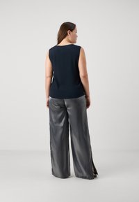 Top senza maniche blu navy con scollo rotondo abbinato a pantaloni larghi argentati a vita alta, lucidi, caratterizzati da spacchi laterali e dettagli in metallo.
