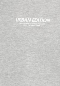 Lichtgrijze stof met vetgedrukte witte tekst: "URBAN EDITION" en een kleinere tagline eronder, met een gladde, lichtjes textuur.