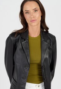 Zwarte leren blazer met een gelapt kraag, twee voorzakken en knoopsluiting. Gepaard met een olijfgroen geribd shirt eronder.