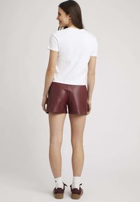 T-shirt blanc à manches courtes et shorts en faux cuir marron. Les shorts ont une texture lisse et un design ajusté, associés à des chaussures montantes.