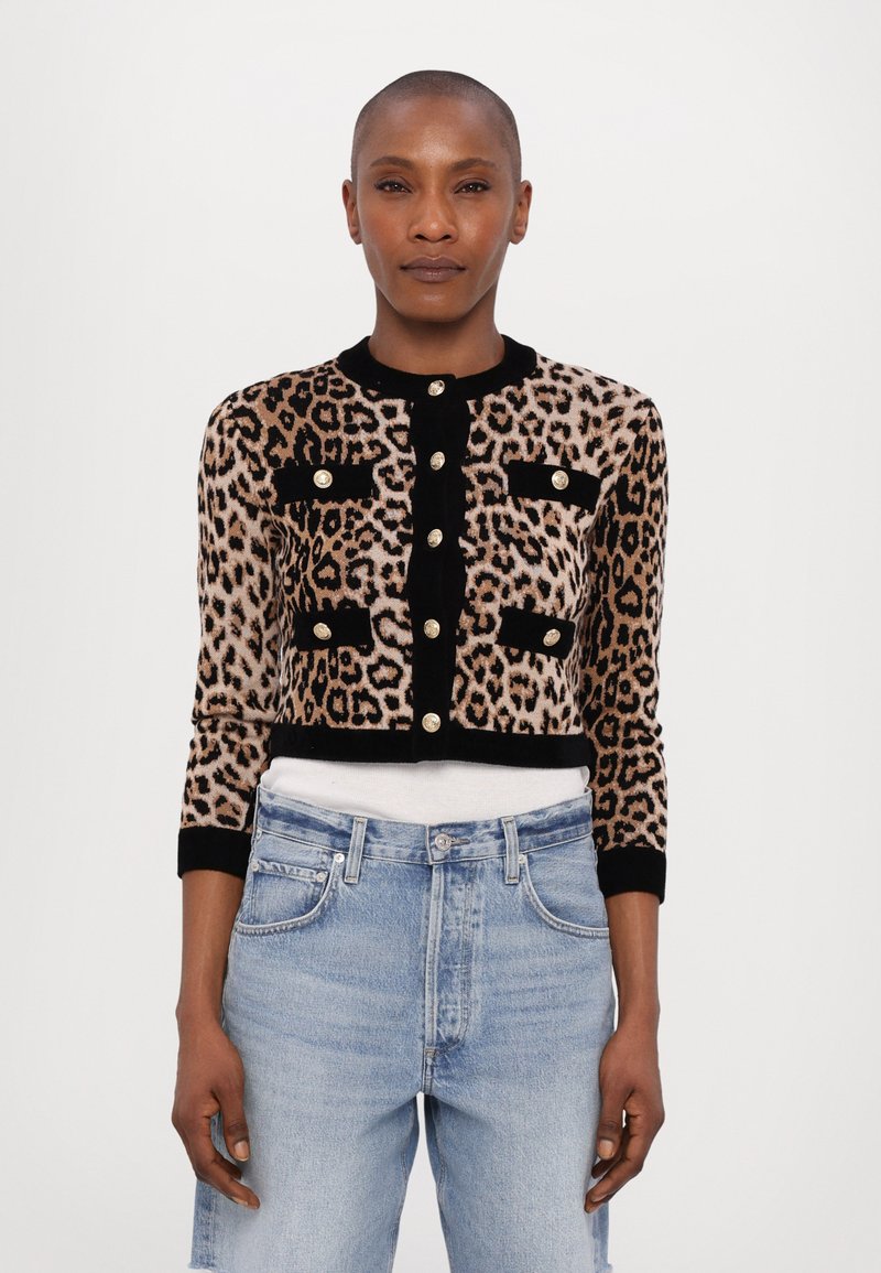 Cardigan scurt cu imprimeu de leopard dintr-un material moale, având accente negre și nasturi aurii, asortat cu blugi din denim de culoare albastră deschisă, cu talie înaltă.