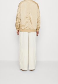 Chaqueta bomber de satén beige con puños y bajo de canalé, combinada con pantalones de rayas anchos en color crema. Textura suave y corte relajado.