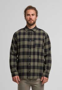 Grün-schwarz kariertes Flanellhemd mit langen Ärmeln, einem Button-Down-Kragen, einer Brusttasche und einem leicht abgerundeten Saum.