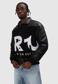 Czarna skórzana kurtka z białym, miękkim przodem ozdobionym dużymi graficznymi napisami. Projekt dopełniają zatrzaski i ściągacze na mankietach.