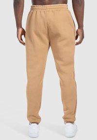 Beige Sweatpants mit einem elastischen Bund, schmal zulaufenden Beinen und seitlichen Taschen, kombiniert mit weißen Sneakers. Baumwollmaterial mit einer weichen Textur.
