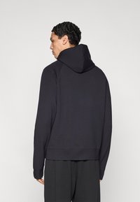 Μαύρο φούτερ με κουκούλα και κορδόνι, μανίκια ράγκλαν και άνετη εφαρμογή. Λείο υλικό και ριμπ μανσέτες. Απλός σχεδιασμός χωρίς διακοσμητικά.