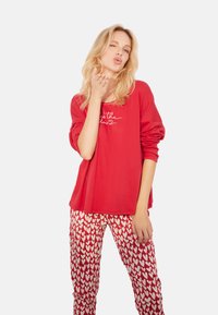 Czerwona bluzka z długim rękawem z białym napisem, w połączeniu z białymi spodniami pidżamowymi z wzorem serc. Miękki materiał o luźnym kroju.