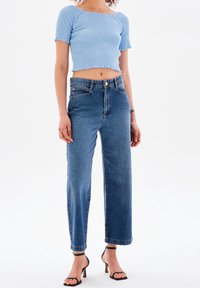 Světle modrý, žebrovaný, zkrácený top s krátkými rukávy, spárovaný s vysokým pasem, rovnými tmavomodrými džíny. Černé sandály na podpatku.