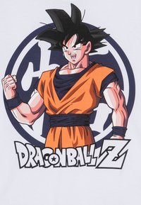 Fehér póló, amelyen egy izmos karakter látható narancssárga és fekete öltözetben, fekete övvel, felirata: "DRAGON BALL Z."