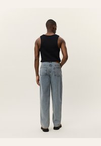 Black sleeveless top paired with light blue wide-leg jeans. The jeans feature back pockets and a subtle faded texture. Black footwear completes the outfit.