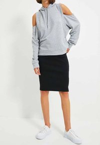 Šedá mikina s odkrytými rameny a dlouhými rukávy, se šňůrkovou kapucí, spojená s černou hladkou tužkovou sukní a bílými teniskami.