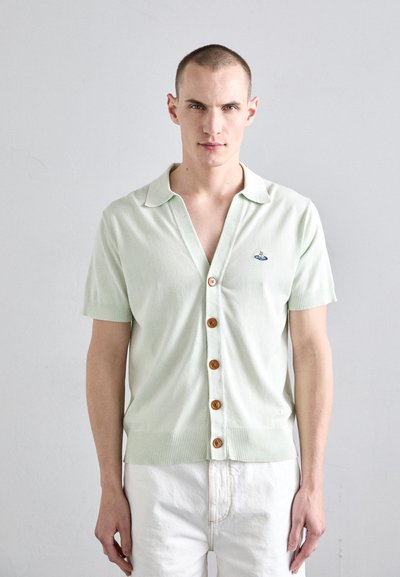 Cardigan corto a maniche corte verde chiaro con vestibilità rilassata, caratterizzato da un orlo a coste, cinque bottoni in legno e un dettaglio ricamato sul petto.