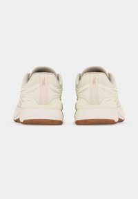 Ζεύγος μπεζ αθλητικών παπουτσιών με υφή στη φτέρνα και καφέ ελαστικές σόλες, εμφανιζόμενα από πίσω σε λευκό φόντο.