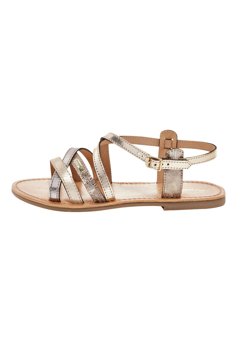 Sandalias planas metálicas de oro y plata con tiras, que cuentan con una correa ajustable en el tobillo y una plantilla de cuero suave.