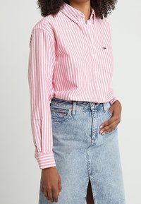 Roze en wit gestreepte blouse met lange mouwen en een borstzak, gecombineerd met een lichtblauwe denim rok met een split aan de voorkant.