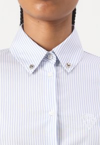 Striped button-up skjorte med lyseblå og hvite vertikale striper, spiss krage og detaljer i sølvfarge. Brodert logo på brystet.