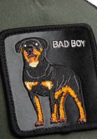 Parche bordado de un perro Rottweiler negro y tostado con el texto "BAD BOY" sobre un fondo de tela negra y verde oliva.