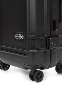 Valigia rigida nera di Eastpak con superficie testurizzata, serratura a combinazione e quattro ruote scorrevoli per una facile manovrabilità.