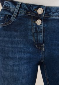 Jeans in denim blu scuro con una texture liscia, dotati di chiusura a doppio bottone, cuciture arancioni e classico design a cinque tasche.