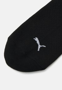 Chaussette noire avec texture côtelée, arborant un petit logo gris clair sur le côté. Design sans couture au niveau des orteils pour un confort optimal.