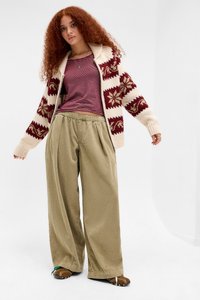 Cardigan lavorato a maglia con motivi floreali bordeaux, base beige chiaro; top a righe sotto; pantaloni larghi verdi oliva; calzature marroni.