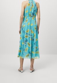 En ärmlös, lätt klänning i ljus turkos med stora gula blommönster, med en åtsittande midja och svängd nederkant.