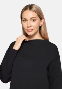 Sweat-shirt noir à coupe décontractée avec un large col. Manches longues avec poignets côtelés et texture de tissu douce. Détails de design minimalistes.