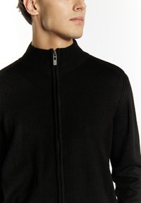 Svart stickad zip-up tröja med hög krage och subtil ribbad struktur. Inkluderar en framdragkedja med en metallisk dragflik.