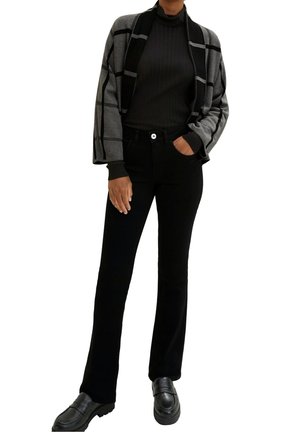 Svarta byxor med vida ben kombinerade med en grå och svart rutmönstrad kofta med ribbad struktur och en figurnära polotröja under. Svarta loafers.