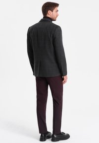 Grå rutiga blazer i texturerad tyg, ihop med mörk vinröda byxor och svarta skor. Bakifrån framhäver den skräddarsydda designen.