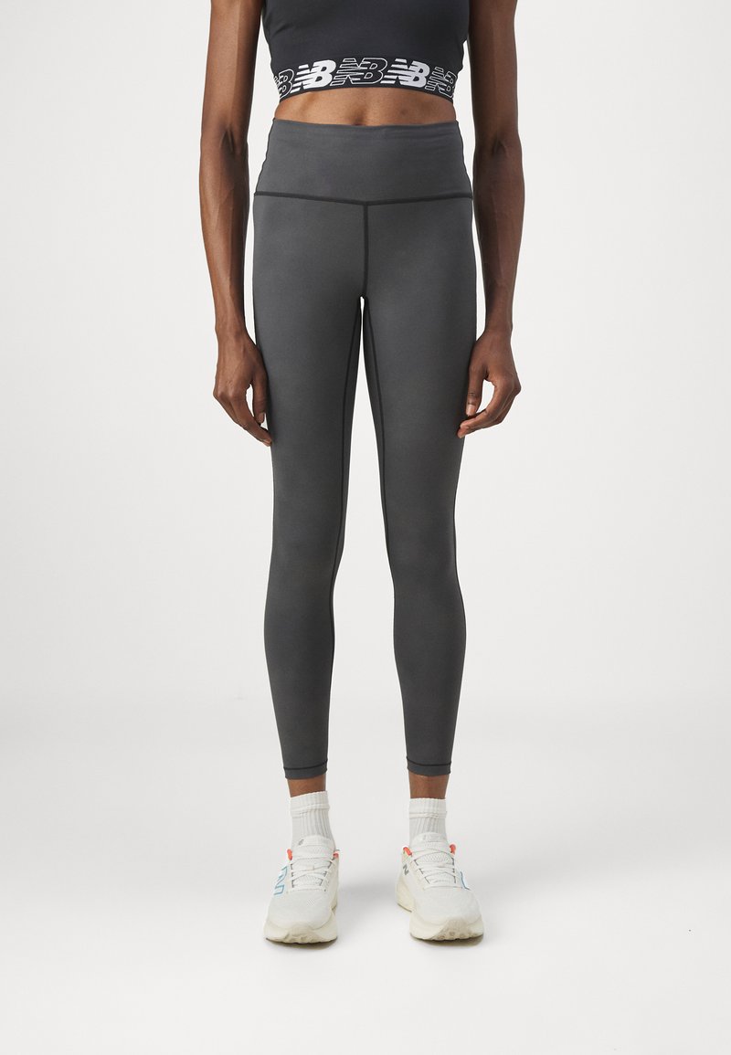 Leggings gris taille haute avec une texture lisse, dotés de coutures contrastantes. Portés avec un haut court noir et des baskets blanches.