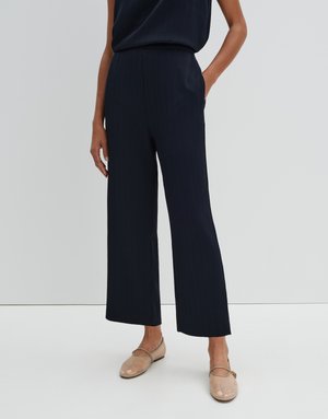 Pantalons larges couleur marine avec un subtil motif à rayures. Fabriqués en tissu texturé, ils présentent une taille haute et des poches sur les côtés. Les chaussures sont des ballerines beige.