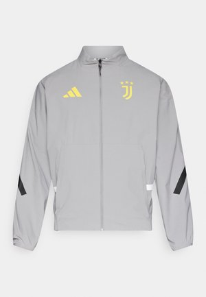 Szara lekka kurtka z zamkiem z przodu, wysokim kołnierzem, czarnymi akcentami na rękawach, żółtymi logo Adidas i Juventusu oraz elastycznymi mankietami.