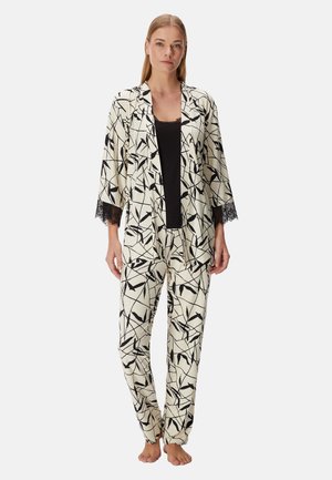 Femme debout pieds nus portant un ensemble de pyjama à motif abstrait noir et blanc avec des manches bordées de dentelle et un haut noir en dessous.
