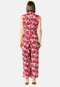 Röd blommig mönstrad jumpsuit med en åtsittande midja, utan ärmar, vida byxor och krage. Slät tygtextur.