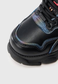 Μαύρο αθλητικό παπούτσι με ιριδίζοντες τόνους και υφή στις λεπτομέρειες. Διαθέτει ελαστική σόλα και ενισχυμένη ραφή. Τα κορδόνια είναι στερεωμένα με μεταλλικά κουμπώματα.