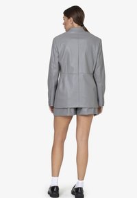 Blazer in finta pelle grigia con una vestibilità strutturata, spacchetto posteriore singolo e polsini con bottone, abbinato a pantaloni corti coordinati, design minimalista.