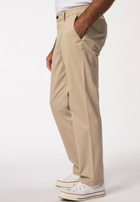 Pantaloni di cotone beige con una vestibilità rilassata, caratterizzati da un cinturino elastico, tasche laterali e una chiusura con bottone. Indossati con sneaker bianche.