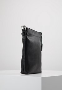 Czarna skórzana torba o zwartej, prostokątnej formie, wyposażona w srebrny pasek z okuciami, teksturowane wykończenie oraz minimalistyczny design.