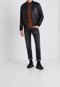 Czarna skórzana kurtka bomber z prążkowymi mankietami, brązowy sweter, ciemne dżinsy oraz czarne trampki. Prosty i nowoczesny design.