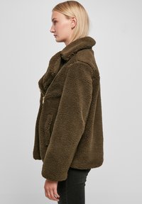 Bruine fleecejack met een pluche textuur, sjawl-kraag en een gouden rits. Heeft een losse pasvorm en zijzakken.