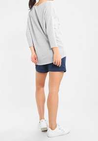 Chemise grise, surdimensionnée, à manches longues, en matière douce, associée à un short bleu marine et des baskets blanches. Tenue simple et décontractée.