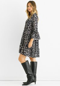 Black and beige leopard print dress with flared sleeves, tiered design, and knee-high black leather boots. Smooth texture and playful pattern.