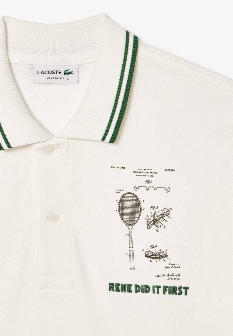 Polo blanc avec col rayé vert, devant boutonné, croquis de brevets de raquettes de tennis, et "RENE L'A FAIT EN PREMIER" brodé en vert.