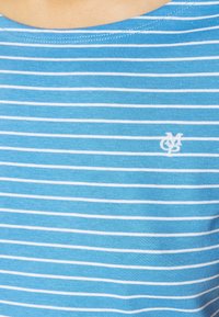 Primer plano de una tela de rayas horizontales azul y blanca con un pequeño logotipo bordado en blanco en el lado derecho.