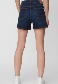 Ciemnoniebieskie szorty dżinsowe z wysokim stanem, z dwoma tylnymi kieszeniami, czystym wykończeniem i szczegółowymi przeszyciami. Noszone z białymi botkami za kostkę.